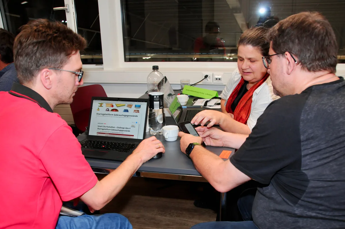 Man sieht drei Menschen an Laptops diskutieren.